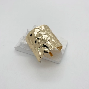 Close-up of golden metal hair hook with irregular hammered texture on a white artistic base