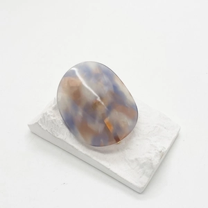 Detailed close-up of oval acetate ponytail hook with blue and amber marbled texture finish
