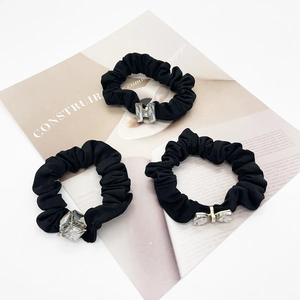 Detail of three black hair ties featuring crystal bow and geometric charms set on a magazine
