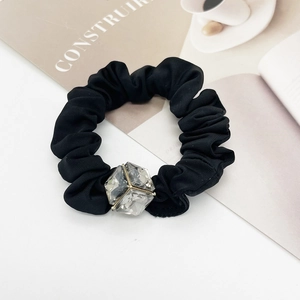 Close-up of a black pleated hair scrunchie featuring a large sparkling faceted crystal