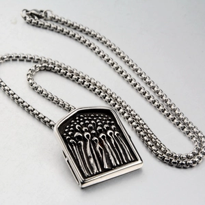 Macro detail of silver rectangular shield pendant with intricate character relief on box chain
