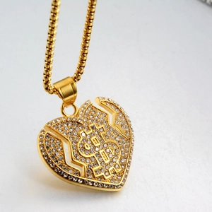Détail du pendentif cœur brisé doré avec signe dollar serti de pierres scintillantes