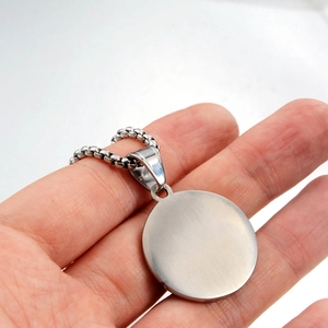 Detailed view of Tree of Life pendant necklace in brushed stainless steel held by hand