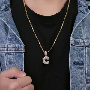 Modella che indossa una collana dorata con ciondolo lettera C e pavé di zirconi luminosi