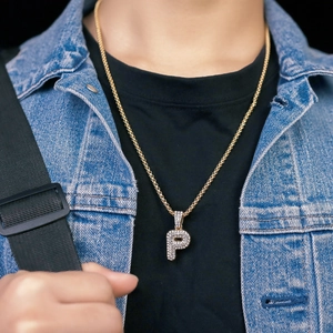 Dettaglio della collana dorata con ciondolo lettera P e strass indossata da una modella