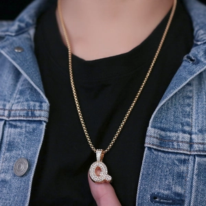 Dettaglio della collana dorata con ciondolo lettera Q e cristalli lucenti su una modella