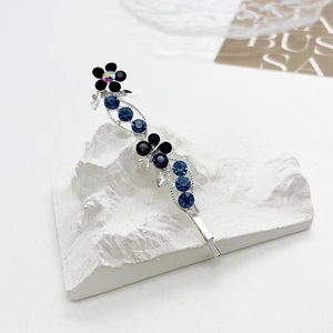 Détail de la barrette argentée avec strass bleus et fleur noire sur support en pierre