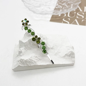 Détail d'une pince à cheveux argentée avec feuilles de cristal vert et strass aurore