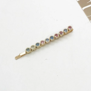Close-up of golden bobby pin with ten multicolored round rhinestones on white base