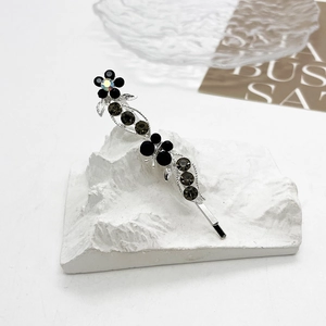 Détail d'une barrette argentée avec fleur noire, papillon et strass étincelants