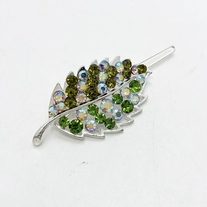 Detailed close-up of leaf-shaped hair clip with green rhinestones on silver metal base