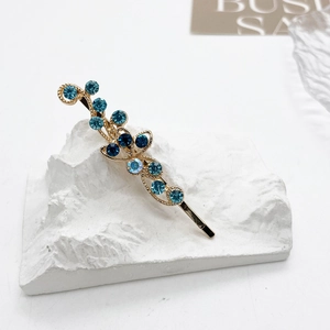 Détail de la barrette dorée à fleurs ornée de strass bleus sur un piédestal blanc