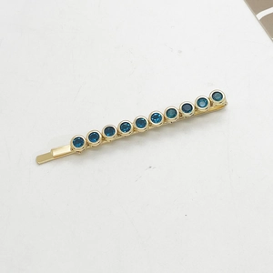 Close-up of golden hair clip with ten round dark blue rhinestones on grey background