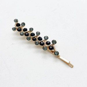 Detail of gold bobby pin with grey rhinestones in a wavy pattern over white surface