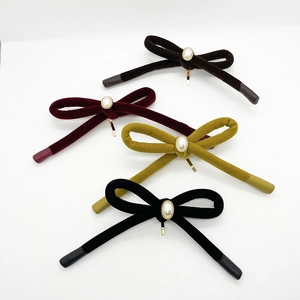 Detail of four velvet bow hair clips with pearl centers in black, red, yellow and brown