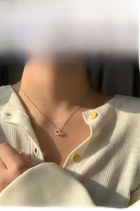 Close-up of minimalist silver circular pendant necklace worn on a white cardigan