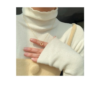 Close-up of a minimalist gold circular pendant necklace on a model wearing white knitwear