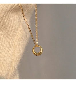 Macro shot of gold circular pendant on fine chain against beige knit background