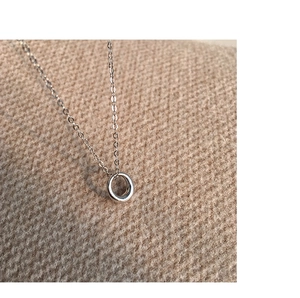 Close-up of a silver minimalist circular pendant necklace on textured knit fabric