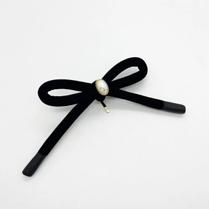Detail view of a black velvet bow hair clip with a large pearl in a gold metal setting