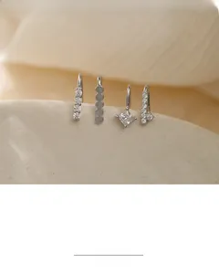 Macro detail of silver layered ear cuffs with cubic zirconia and opal on sand background