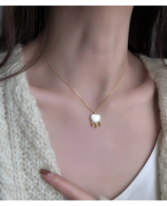 Détail du collier pendentif serrure en nacre sur mannequin avec pompons dorés fins