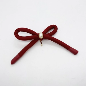 Detail of red fabric bow hairclip featuring a white pearl and golden metal base