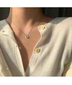 Close-up of minimalist silver round pendant necklace on a female model wearing knitwear