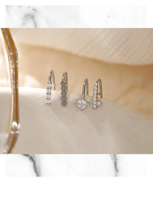 Detailed view of silver asymmetric ear cuffs set with sparkling cubic zirconia on white stand