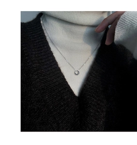 Close-up of a silver minimalist circular pendant necklace worn over a cozy winter knit