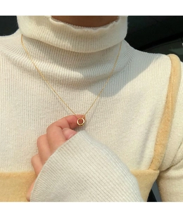 Close-up of minimalist gold circular pendant on fine chain worn with white knitwear