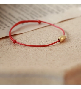 Macro detail of red woven cord bracelet with matte gold bead and adjustable knots