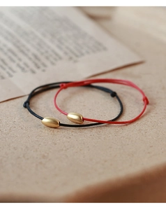 Detail of red and black braided bracelets with matte golden oval bead charms