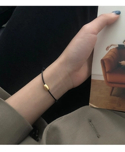 Minimalist black cord bracelet featuring a gold matte bead on a model's wrist detail