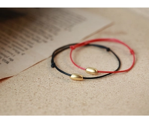 Detail of red and black woven rope bracelets with golden beads on warm background
