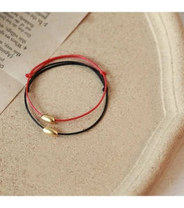 Macro shot of minimalist red and black braided cord bracelets with golden oval bean beads