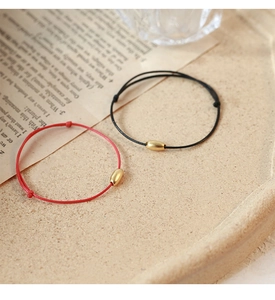Detail showing minimalist woven red and black cord bracelets with golden metal beads