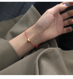 Detail of red string bracelet with a golden oval bead on a wrist against a brown fabric