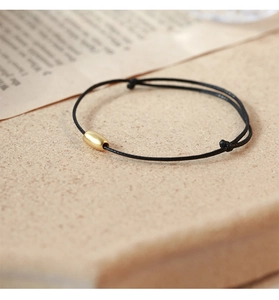 Minimalist woven black cord bracelet with a matte golden bead and adjustable sliding knot