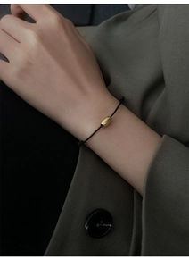 Minimalist black cord bracelet with a matte gold cylindrical bead on a model wrist