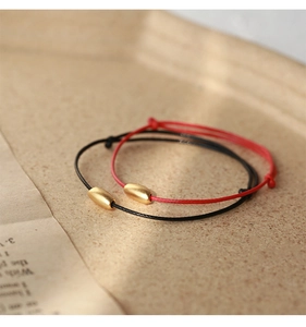 Detail of red and black braided rope bracelets with matte gold beads in a decor tray