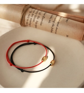 Close-up of minimalist red and black cords with matte gold beads on ceramic plate