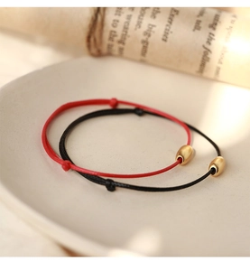 Detail view of adjustable red and black woven bracelets with a golden bead centerpiece