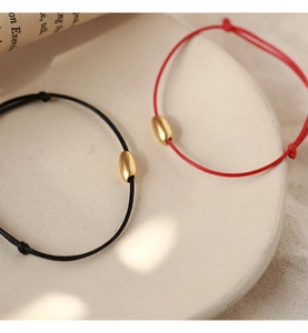 Minimalist red and black braided cord bracelets with matte gold oval beads on ceramic plate