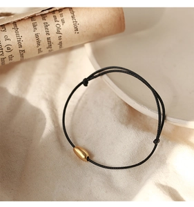 Detail of adjustable black cord bracelet featuring a matte gold oval bead on linen fabric
