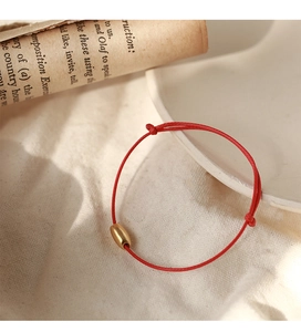 Macro detail of a red woven rope bracelet with a polished golden oval bead on linen