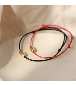 Close-up of minimalist red and black cord bracelets with matte gold capsule beads