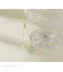 Détail d'un pendentif boucle pingan en jade vert sur une chaîne dorée avec fermoir cœur