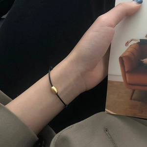 Minimalist black braided bracelet with a matte gold oval bead on a model's wrist