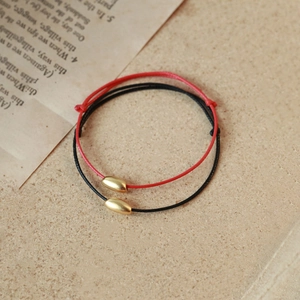 Red and black woven couple bracelets with golden oval beads on vintage paper background
